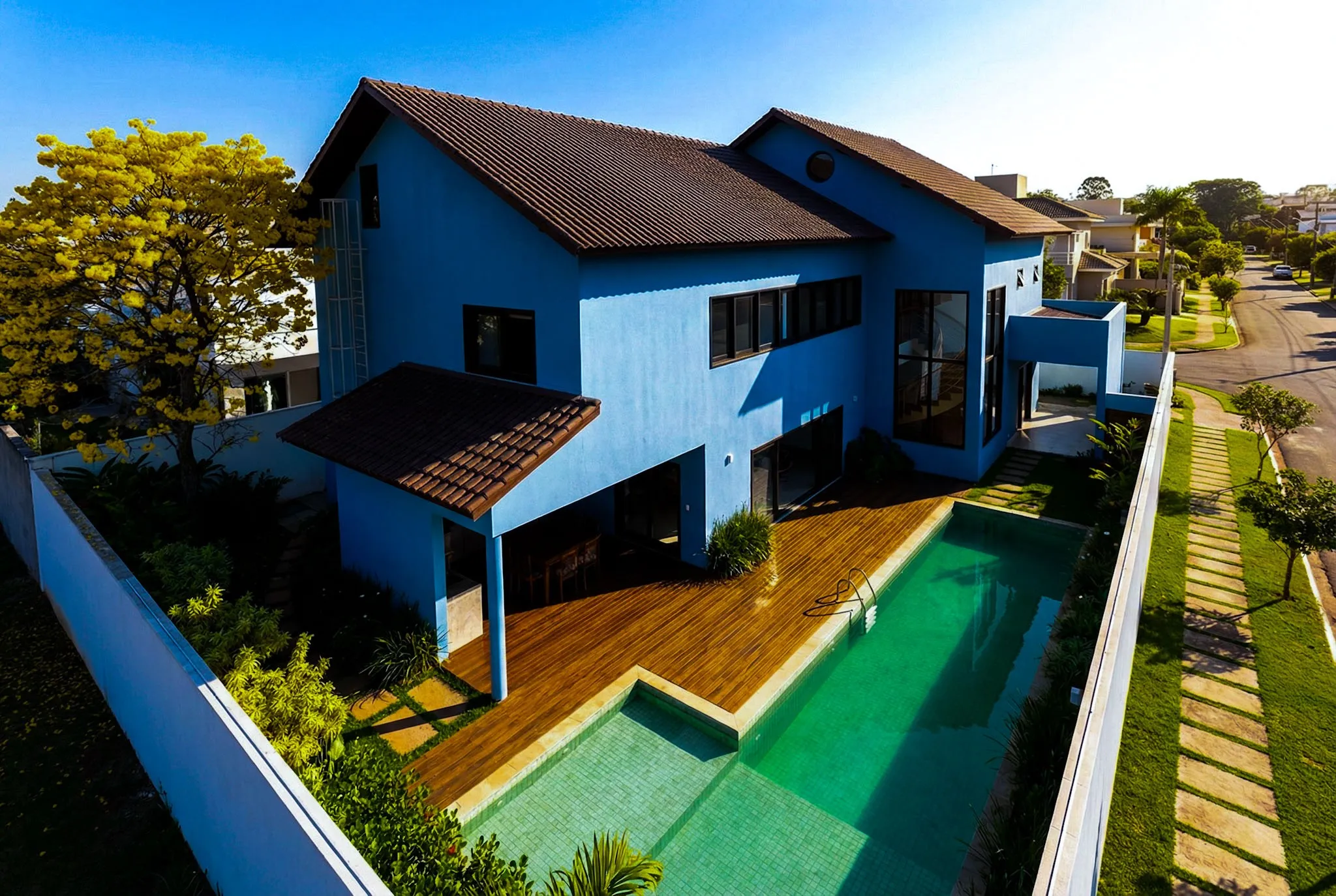 Vista aérea da casa azul, com o deck de madeira e a piscina de raia ao longo do lote.